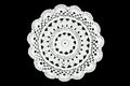 White crocheted coaster lace doily on black background.