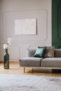 White flowers in big green bottle shape like vase next to grey settee in fashionable living room interior