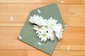 White flowers of chrysanthemum in a green envelope on a wooden background. Spring congratulation gift. Top view, flat