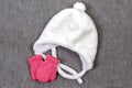 White fluffy children`s hat with ties and pink small mittens. The concept of winter warmth and comfort