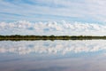 White fluffy clouds in blue sky, reflected on smooth surface of lake surrounded by green trees Royalty Free Stock Photo