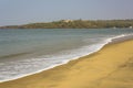 White foam of waves at the yellow sandy beach against the blue sea and rocky beach with green trees and houses Royalty Free Stock Photo