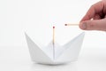 White folded paper boat with unlit match on top and Caucasian male hand and fingers holding another match frontal shot isolated on