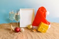 White frame, champagne glasses, christmas balls, Santa hat and gift on sand beach Royalty Free Stock Photo