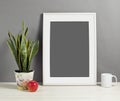 White frame mockup with plant pot, mug and apple on wooden shelf Royalty Free Stock Photo