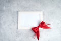 White frame with red bow on grey concrete. Royalty Free Stock Photo