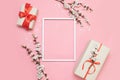 White frame, twigs of flowers with gift boxes on a pink background