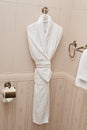 White fresh bath robe hang on bathroom wall. White shower gown and small towels hang in the bathroom stone tiles wall