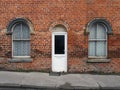 White front door and windows of a typical old brick british terraced house with arched windows and net curtains