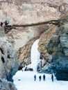 White Frozen waterfall between Mountains. People trekking. Wooden bridge. Zanskar River. Leh Ladakh. India