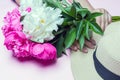 White and fuchsia peonies bouquet and straw hat in female hands isolated on pink background. Flat lay composition, close up.