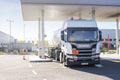 White fuel tanker truck at a petrol station connected by a hose to the underground tanks and refelling it.