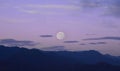 white full moon rising behind a mountain ridge illuminating misty clouds creating a mystical atmosphere. glowing round moon rising Royalty Free Stock Photo