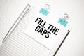White future calculator, paper sheet, pink paper clips and silver colored pen. Text FILL THE GAPS Royalty Free Stock Photo