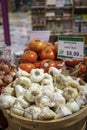 white garlic bulbs for $8.99 per pound in a brown basket surrounded by vibrant red tomatoes and shallot onions