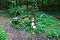 A white gas container with a face painted on it with a doll body laying on a tree trunk surrounded by lush green plants and trees