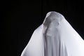 White ghost in white cloth on isolated black background. Face devil shouting covered curtain on blank. Halloween concept