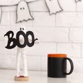 White ghost figure holding word boo near black cup with tea