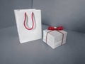 White gift bag with red handles and a white square box with red bow. Mockup box and paper package for overlaying a pattern,