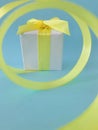 White gift box at the end of the spiral yellow ribbon, blue background, vertical. Royalty Free Stock Photo