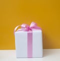 White gift box with pink ribbon isolated on orange background. Royalty Free Stock Photo