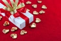 White gift box with red and gold ribbon, and a small gold hearts shape on a red velvet floor, Valentine\'s day Royalty Free Stock Photo