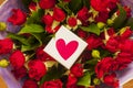 White gift box with red heart on the background of bouquet of red roses in purple wrapping paper. Valentine.