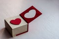 White gift box with a red heart on the lid for a romantic gift for girls on a painted wooden surface.