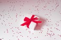 White gift box with red satin ribbon and bow on a white background with confetti Royalty Free Stock Photo