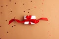 White gift box with a red satin ribbon bow tied on brown background with red stars shapes.Christmas Holidays and present concept Royalty Free Stock Photo