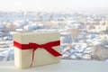 White gift box tied with a red ribbon on the background of the city. Horizontal composition with copy space. Great for Christmas Royalty Free Stock Photo