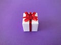 White gift box red ribbon bow on purple background, centre. Royalty Free Stock Photo