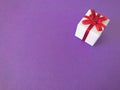 White gift box red ribbon bow on purple background, copy space. Royalty Free Stock Photo