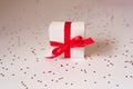 White gift box tied with a red satin ribbon with a bow on a white background with confetti. Valentine`s day Royalty Free Stock Photo