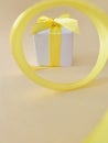 White gift box at the end of the spiral yellow ribbon, off white background , vertical. Royalty Free Stock Photo