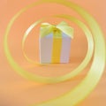 White gift box at the end of the spiral yellow ribbon, orange background, square. Royalty Free Stock Photo