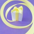 White gift box at the end of the spiral yellow ribbon, purple background, square. Royalty Free Stock Photo