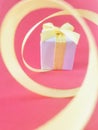 White Gift box at the end of the spiral yellow ribbon, pink background, vertical. Royalty Free Stock Photo