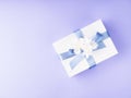 White gift box wrapped with blue ribbon and decor flowers on purple Royalty Free Stock Photo