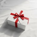 A white gift box wrapped with a shiny red ribbon and bow, placed on a white Royalty Free Stock Photo
