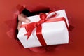 White gift with red ribbon being delivered or giving through a red torn paper background