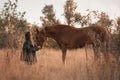 A white girl in leather jacket, black glasses next to a horse and poses in the forest at sunset, like in a fairy tale Royalty Free Stock Photo