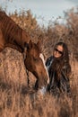 A white girl in leather jacket, black glasses next to a horse and poses in the forest at sunset, like in a fairy tale Royalty Free Stock Photo