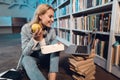 White girl near bookshelf in library. Student is eating apple from lunchbox. Royalty Free Stock Photo