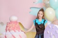 White girl 10 years old among huge sweets, balloons on a pink background