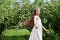 White girl 11 years old with long hair in a white dress whirls and laughs in a blooming garden