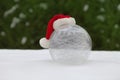 white glass ball on snow with christmas hat. winter world near Christmas tree. snowy background. Royalty Free Stock Photo