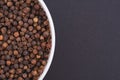 White glass bowl of black pepper. Isolated on a dark grey background.