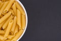 White glass bowl of raw penne rigate pasta. Isolated on a dark grey background. Royalty Free Stock Photo