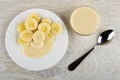 White plate with slices of banana and condensed milk, bowl with milk, spoon on wooden table. Top view Royalty Free Stock Photo
